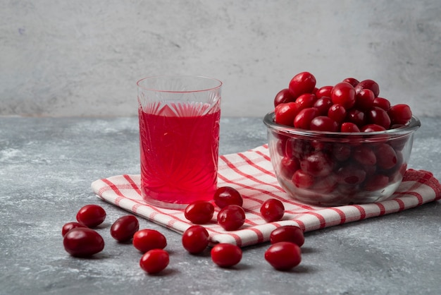 Kostenloses Foto rote kornelkirschen in der glasschale auf kariertem handtuch mit einem glas saft.