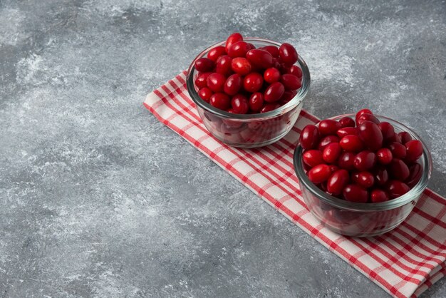 Rote Kornelkirschen in der Glasschale auf kariertem Handtuch.