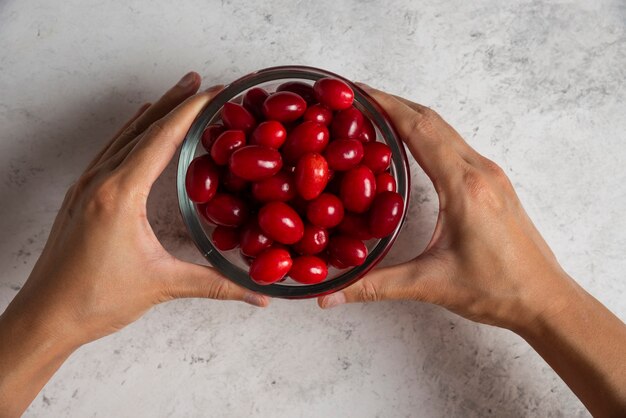 Rote Kornelkirschen in der Glasschale in der Hand einer Person.