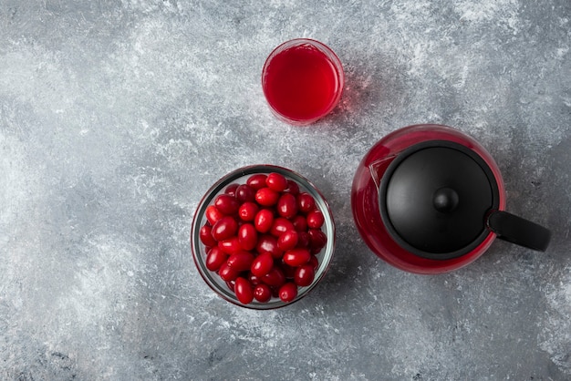 Rote Kornelkirschen in einer Glasschale mit Saft im Wasserkocher und im Glas.