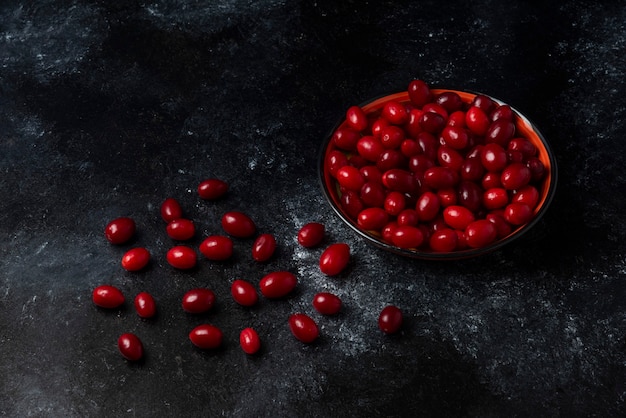 Rote kornelkirschen in einer tasse auf schwarzer oberfläche.