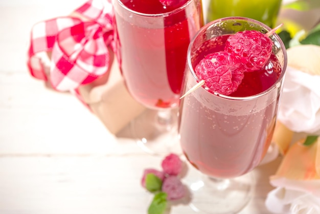 Rote mimosen-cocktail zum valentinstag. klassisches mimosengetränk mit himbeersaft, himbeer- und minzdekor. mit geschenkbox zum valentinstag, rosenblüten, champagnerflasche