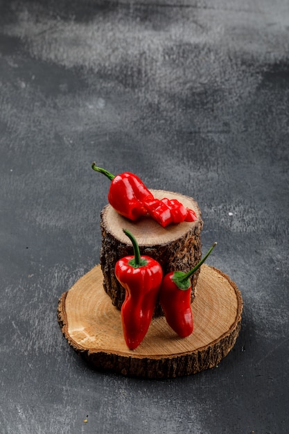 Rote Paprika mit Holzstücken auf grungy grauer Wand, hohe Winkelansicht.