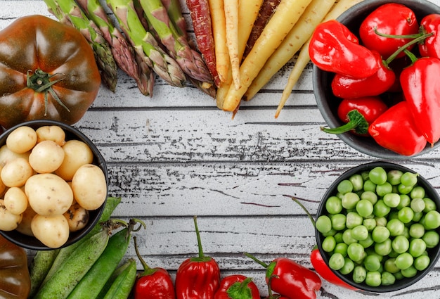 Rote Paprika mit Kartoffeln, Tomaten, Spargel, grünen Schoten, Erbsen, Karotten in einer Schüssel auf Holzwand, Draufsicht.