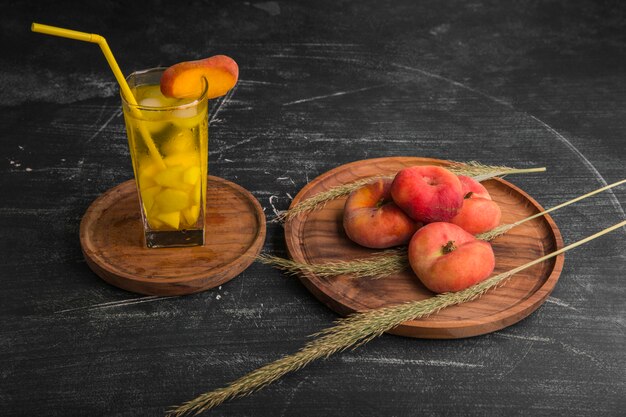 Rote Pfirsiche mit einem Glas Saft in einer Holzplatte