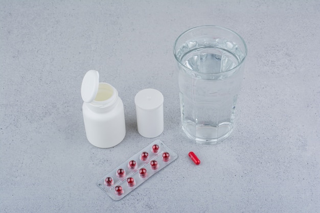 Rote Pillen, Behälter und Glas Wasser auf Marmoroberfläche.