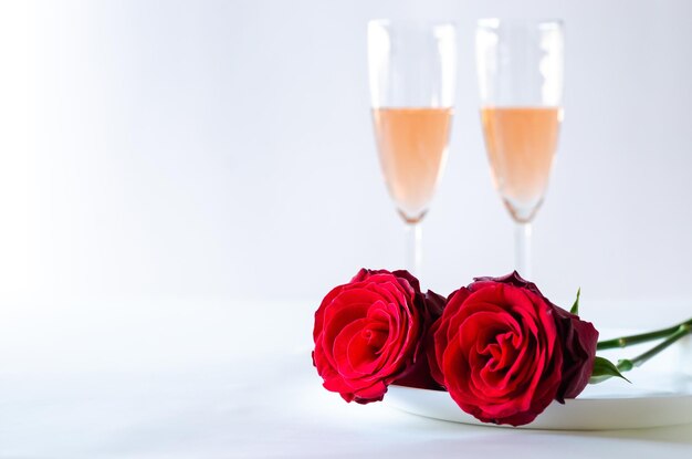 Rote rosen auf teller mit gläsern sekt auf weißem hintergrund zum jubiläum und valentinstag-konzept.