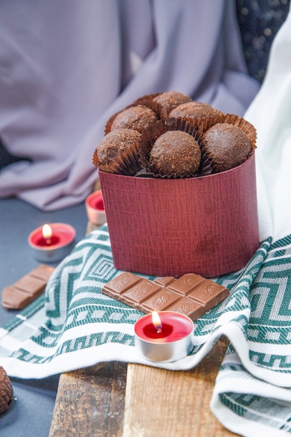 rote Schachtel Pralinen, milchige Tafel und brennende Kerzen auf einem Stück Holz