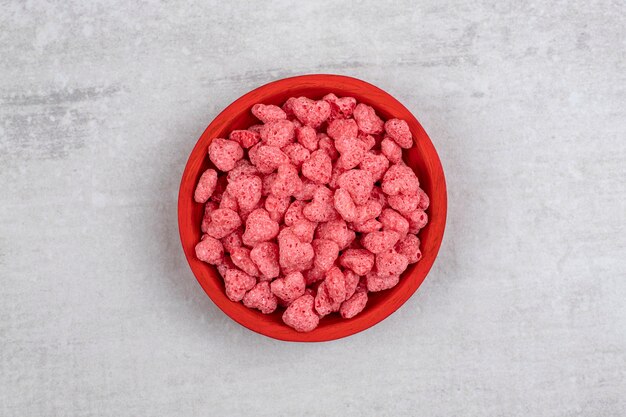 Rote Schüssel voll von rosa Müsli auf Steintisch.