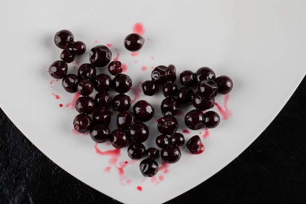 Rote schwarze Johannisbeere in einem weißen Teller auf Schwarz.