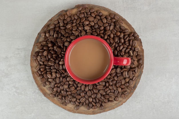 Rote Tasse Kaffee mit Kaffeebohnen auf Holzstück