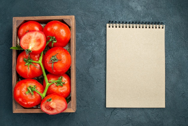 Rote Tomaten der Draufsicht in Holzkiste-Notizbuch auf schwarzem Tisch