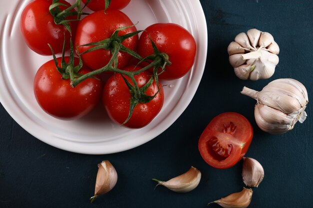 Rote Tomaten in der weißen Platte mit Knoblauchhandschuhen. Ansicht von oben.