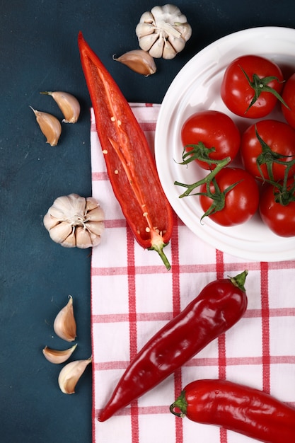 Rote tomaten in einer weißen platte auf einem blauen backgorund auf einem überprüften tuch.