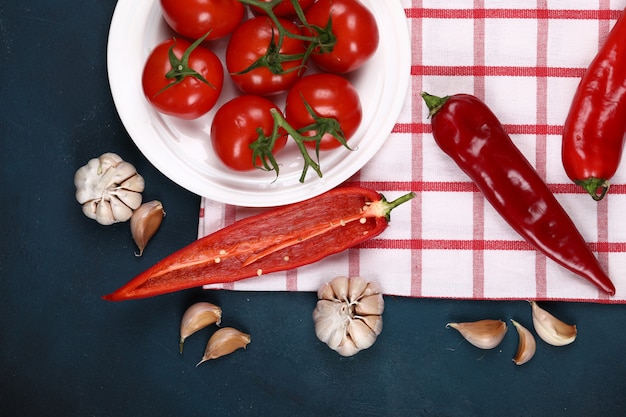 Rote Tomaten in einer weißen Platte auf einem überprüften Tuch mit Paprikas und Knoblauch.