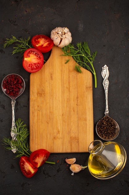 Rote Tomaten zusammen mit grünen Knoblauchscheiben und Öl umgeben von gelbem Holzschreibtisch