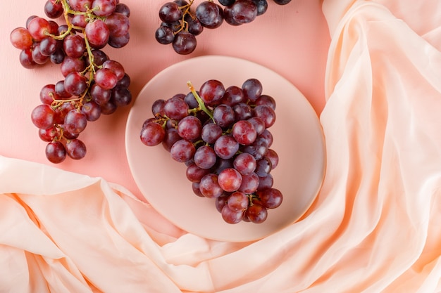 Rote Trauben in einer flachen Platte lagen auf Rosa und Textil