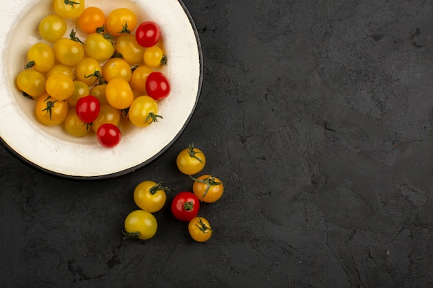 Kostenloses Foto rote und gelbe frische reife bunte tomaten innerhalb der weißen platte auf einem grauen boden