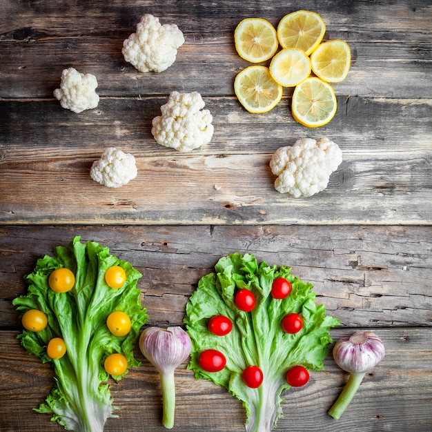 Rote und gelbe Tomaten der Draufsicht mit Salat, Blumenkohl, Zitronen, Knoblauch auf dunklem hölzernem Hintergrund.