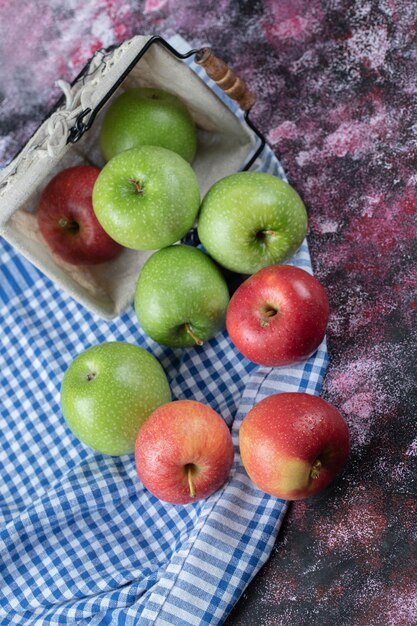 Rote und grüne Äpfel aus einem Korb auf kariertem Tuch heraus.