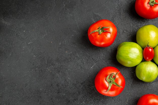 Rote und grüne Tomaten der Draufsicht um eine Kirschtomate rechts von dunklem Grund mit Kopierraum