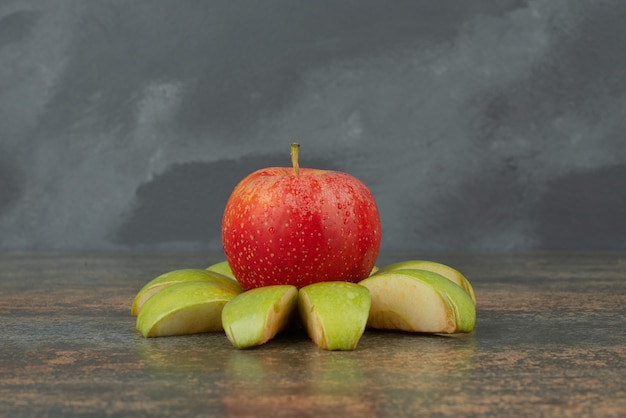 Roter Apfel mit Apfelscheiben auf Marmoroberfläche.