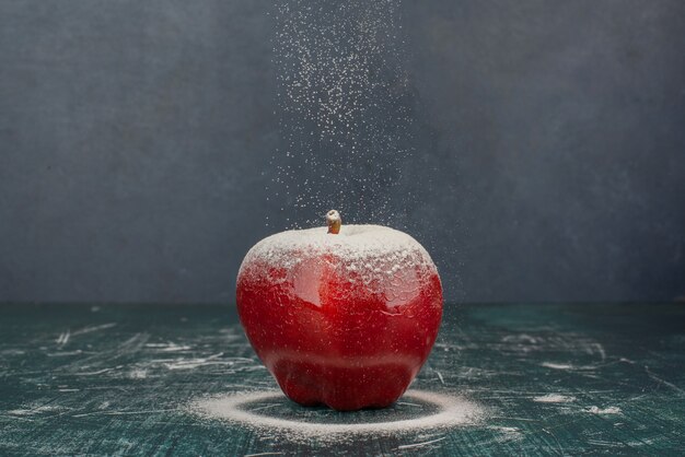 Roter Apfel verziert mit Pulver auf blauem Hintergrund.