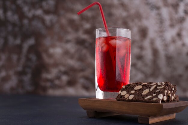 Roter Cocktail mit Eiswürfeln in einem Glas mit einem Stück Kuchen beiseite