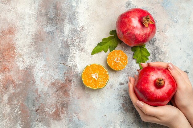 Roter Granatapfel der Draufsicht in den Zitronenscheiben der weiblichen Hand auf freiem Raum der nackten Oberfläche