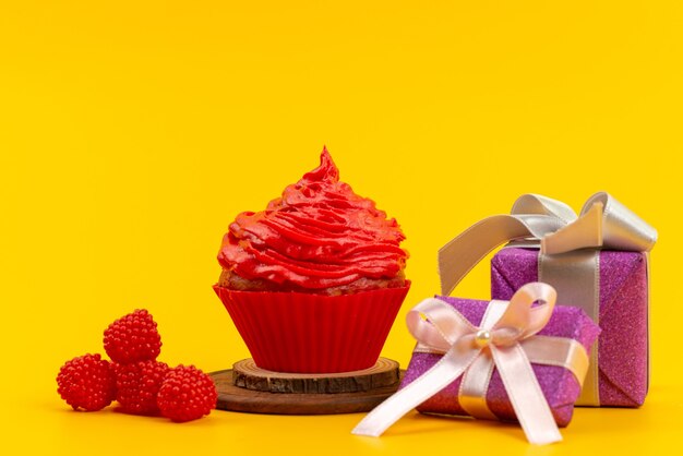 Roter Kuchen der Vorderansicht mit frischen roten Himbeeren und lila Geschenkboxen auf gelbem Schreibtisch