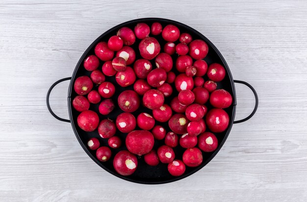 Roter Rettich in einer schwarzen Pfanne auf weißem Holztisch. flach liegen.