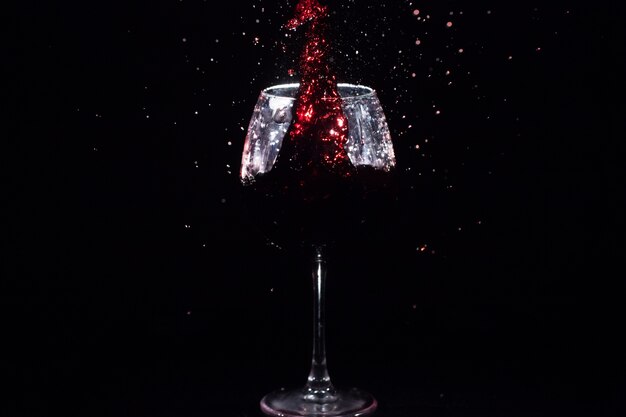 Roter Saft spritzt in einem Kristallglas, das im schwarzen Raum steht