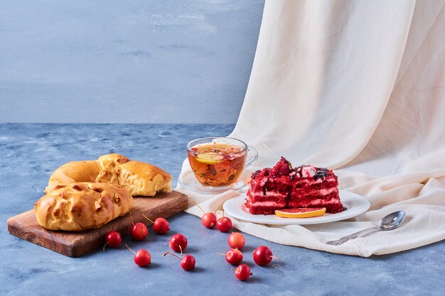 Roter Samtkuchen mit Brötchen und Tee auf einem Holzbrett auf Blau