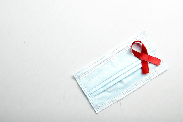 Rotes Band und Gesichtsmaske mit weißem Hintergrund. Bewusstsein für das HIV-Aids-Band
