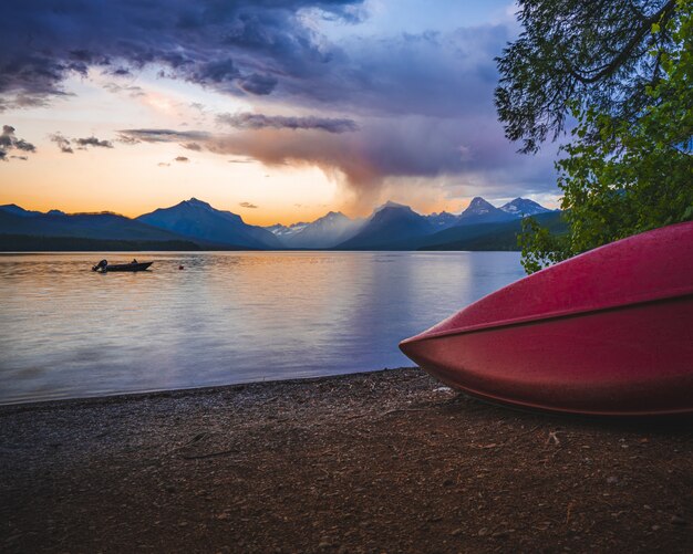 Rotes Boot nahe dem Meer, umgeben von schönen Bergen unter dem Sonnenuntergangshimmel