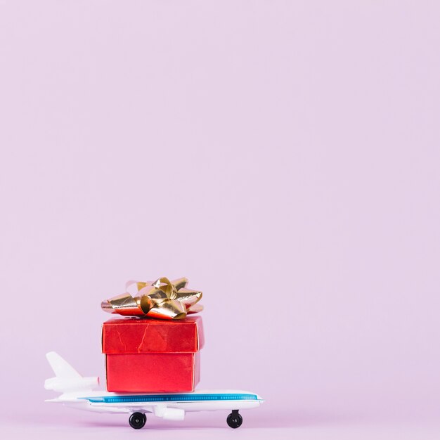 Rotes giftbox mit goldenem Bogen über dem Spielzeugflugzeug gegen rosa Hintergrund