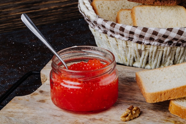 Rotes Kaviarglas der Seitenansicht mit Weißbrot und Walnuss auf einem Brett