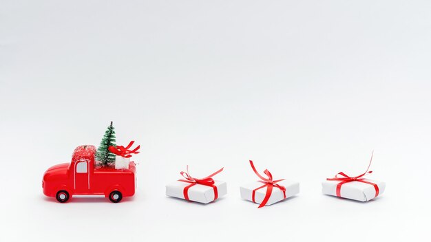 Rotes Spielzeugauto mit Weihnachtsbaum darauf und Geschenken. Blauer Hintergrund