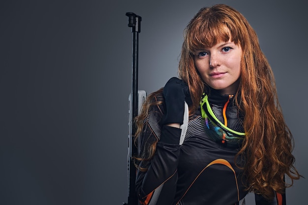 Rothaarige Biathlon-Meisterin, die mit einer konkurrenzfähigen Waffe in einem Studio auf grauem Hintergrund zielt. Rothaarige Biathlon-Meisterin, die mit einer konkurrenzfähigen Waffe in einem Studio auf grauem Hintergrund zielt.