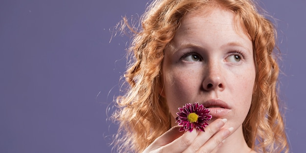 Rothaarige Frau, die eine Blume nahe ihrem Mund mit Kopienraum hält