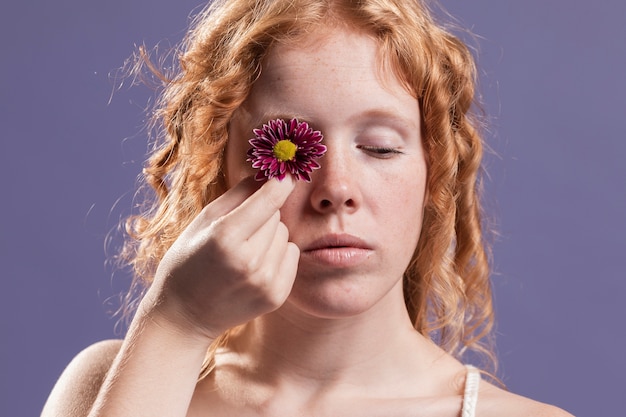 Rothaarige Frau, die eine Blume über ihrem Auge hält