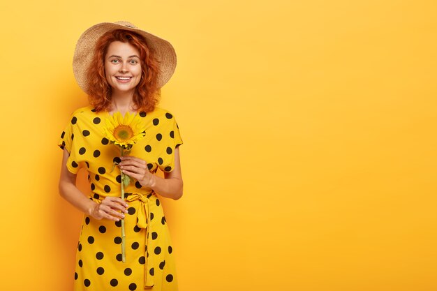 rothaarige Frau, die im gelben Polka-Kleid und im Strohhut aufwirft