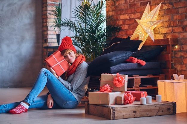 Rothaarige Frau hält ein Weihnachtsgeschenk in einem Wohnzimmer mit Loft-Interieur.
