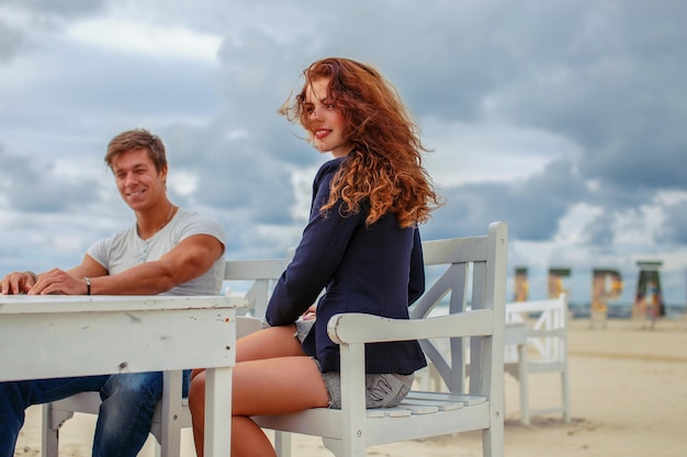 Rothaarige Frau und ein Typ sitzen am Tisch am Strand.