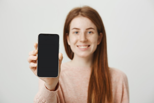 Rothaarige Teenager-Mädchen zeigt Smartphone-Anzeige