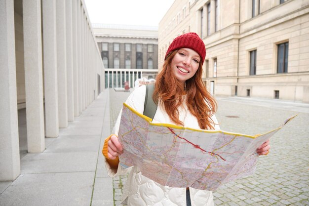 Rothaarige Touristin erkundet die Stadt und sieht sich die Papierkarte an, um den Weg für historische Sehenswürdigkeiten zu finden