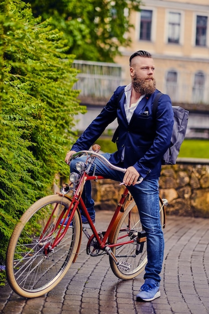 Rothaariger bärtiger Mann in blauer Jacke und Jeans auf einem Retro-Fahrrad in einem Park.