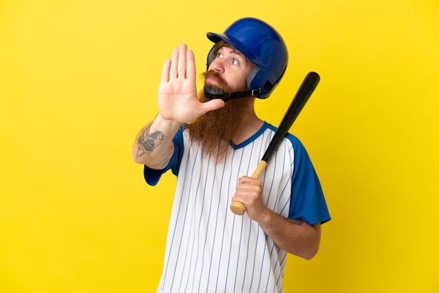 Rothaariger baseballspieler mit helm und schläger isoliert auf gelbem hintergrund, der stop-geste macht und enttäuscht Premium Fotos
