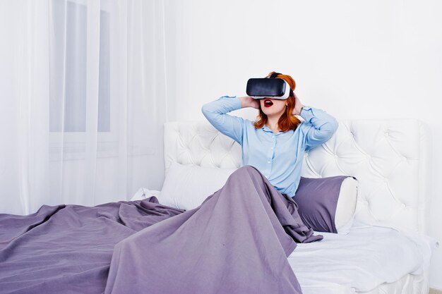 Rothaariges Mädchen im Bett mit VR-Brille im Studiozimmer