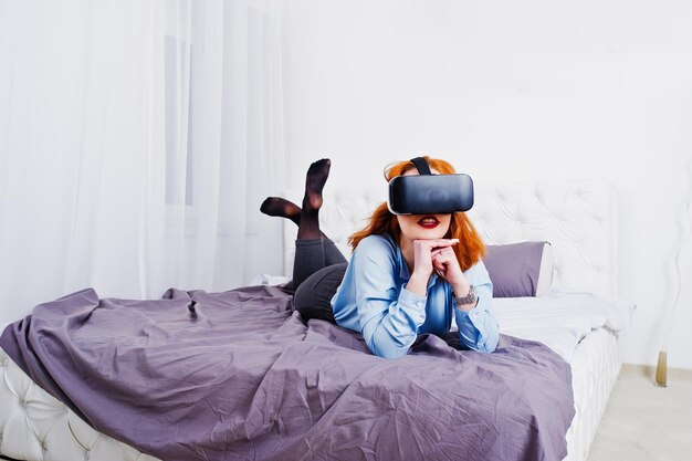 Rothaariges Mädchen im Bett mit VR-Brille im Studiozimmer